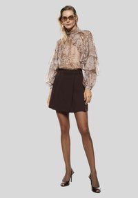 Blusa trasparente color marrone chiaro con dettagli a volant e stampa astratta, abbinata a una minigonna nera aderente. Scarpe con tacco alto nere completano il look.