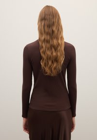 Long-sleeve brown top made from ribbed fabric, fitted design, with a round neckline and a smooth texture, worn with a matching skirt.