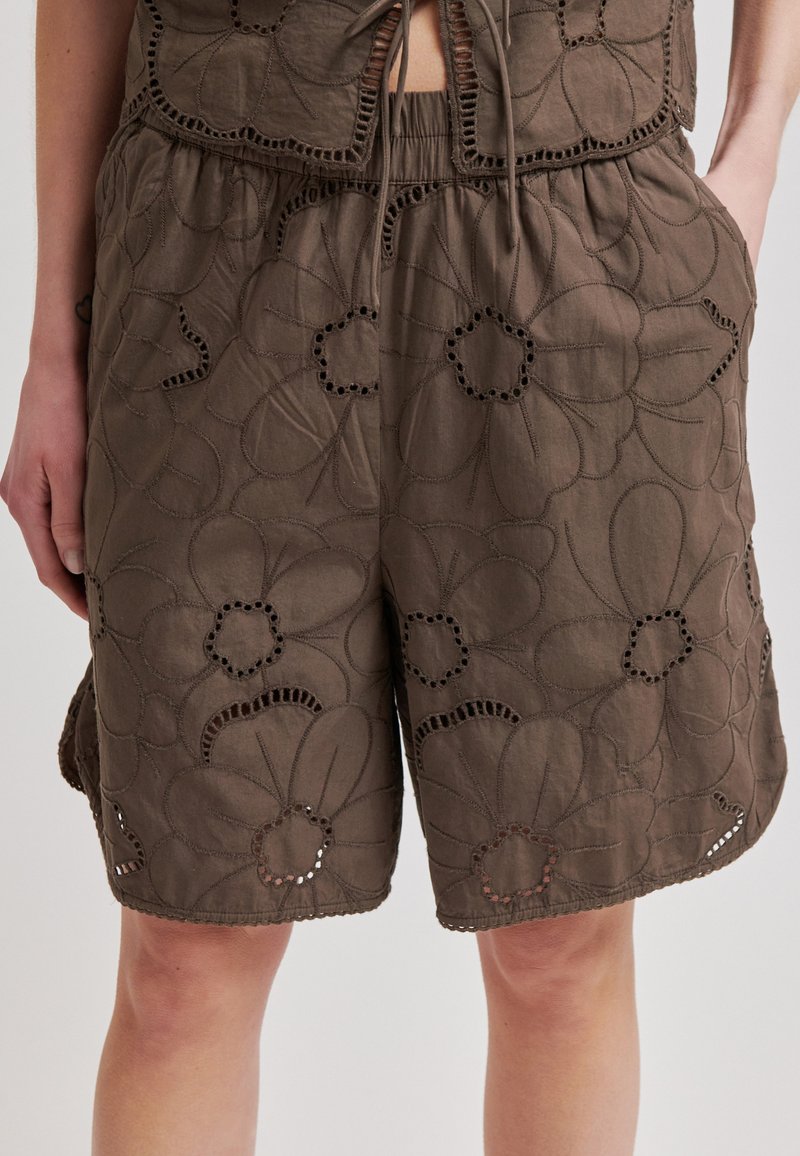 Shorts amples marron avec une grande broderie florale et des découpes, portés avec un crop top assorti noué.