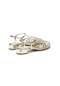 Las sandalias de metal dorado presentan un diseño abierto con múltiples correas, una suela plana y un tacón bajo y modesto. Acabado suave con una textura brillante.