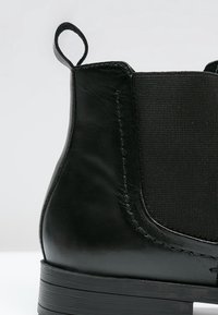 Botín negro de cuero con paneles laterales elásticos, superficie texturizada y un tirador. Presenta una suela plana y duradera para mayor estabilidad.