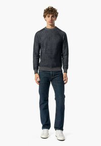 Maglione a coste grigio scuro con collo rotondo e maniche raglan, abbinato a jeans blu e sneakers bianche. Design semplice e tessurato.
