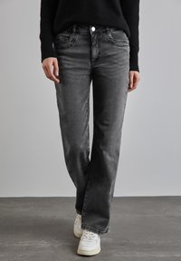 Jeans en denim gris avec une coupe décontractée, dotés de poches avant, de détails de couture subtils et d'une fermeture à bouton classique. Portés avec des baskets blanches.