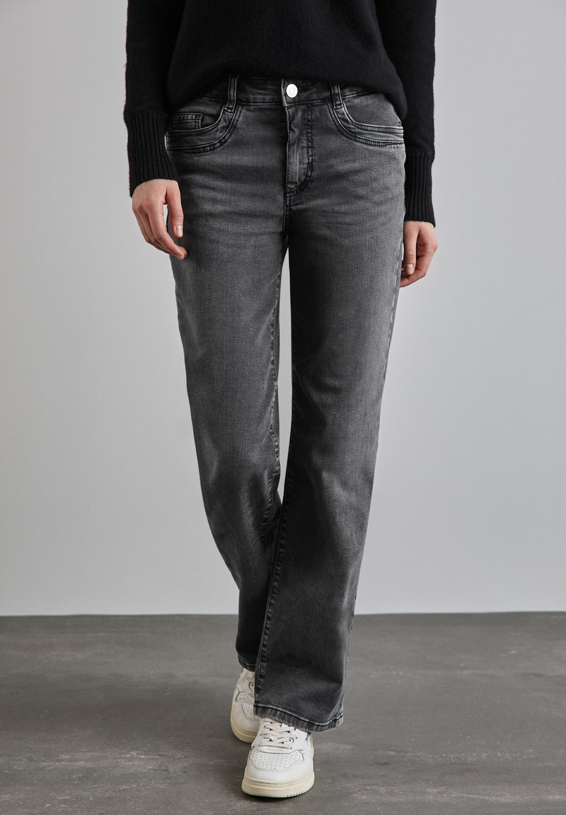 Jeans en denim gris avec une coupe décontractée, dotés de poches avant, de détails de couture subtils et d'une fermeture à bouton classique. Portés avec des baskets blanches.