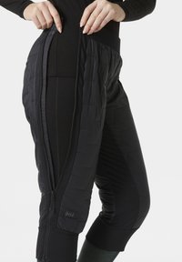 Zwarte geïsoleerde broek met een ritssluiting, gemaakt van textuurstof, met een aansluitende tailleband en een logo-label aan de zijkant.