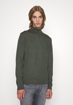 Grüner Rollkragenpullover aus einem weichen, strukturierten Strickstoff. Mit langen Ärmeln und figurnaher Passform, kombiniert mit grauen Jeans.