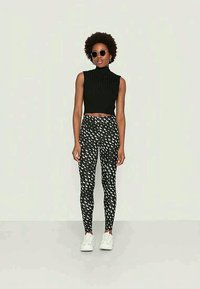 Top preto, canelado e sem mangas, emparelhado com leggings de cintura alta com um padrão de lua crescente branca. Modelo usa óculos de sol redondos e sapatilhas brancas.