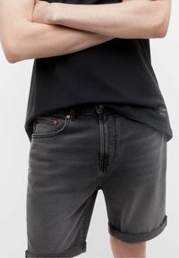 Pantalones cortos de denim gris con dobladillos enrollados, que presentan remaches de cobre, un diseño ajustado y una camiseta negra lisa. Apariencia simple y casual.