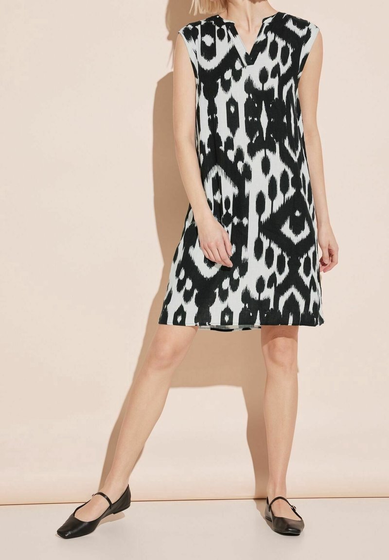 Robe sans manches noire et blanche à motifs, longueur genou, portée avec des ballerines noires style Mary Jane sur un mannequin debout.
