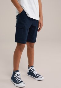 Shorts cargo bleu marine avec poches latérales et coupe décontractée, associés à des baskets montantes bleu marine avec des lacets blancs et des semelles en caoutchouc.
