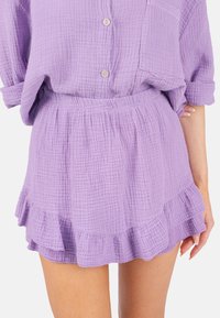 Lila, strukturierte Stoffbluse mit Knöpfen und einer Tasche, kombiniert mit einem passenden Volantrock, der einen elastischen Bund und ein schichtartiges Design aufweist.