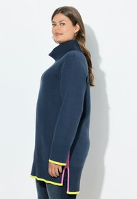 Maglione a collo alto blu navy con texture a coste, maniche lunghe e fessure laterali; accentuato da bordi gialli e rosa all'orlo e ai bordi delle fessure.