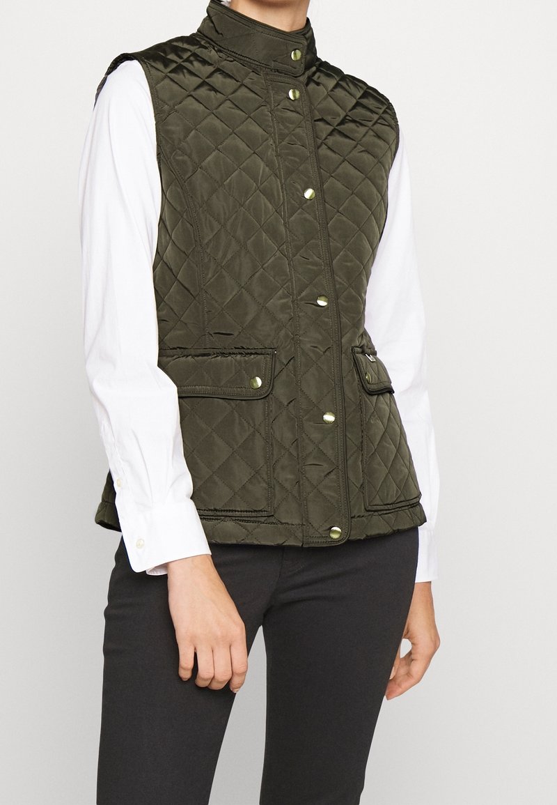 Rutig grön väst med hög krage, guldknappar, och två framfickor. Bärs över en vit skjorta med en slät textur.