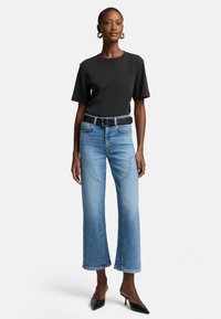 Svart t-shirt med kort ärm i kombination med ljusblå vida jeans, iförd ett svart bälte och svarta klackskor med spetsig tå.