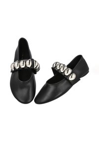 Zapatos planos de cuero negro con punta redondeada y una correa con cinco detalles metálicos. Textura lisa con un diseño minimalista.