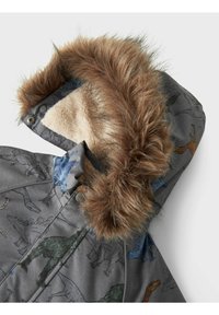 Grå polstret jakke med en hætte i kunstpels, der har flerfarvede dinosaurtryk og en cremefarvet tekstur indvendigt. Synlige accentknapper.