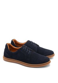 Zapatos de ante azul marino con parte superior perforada, suela de goma marrón y diseño de cordones. El interior presenta un forro en contraste de color naranja.