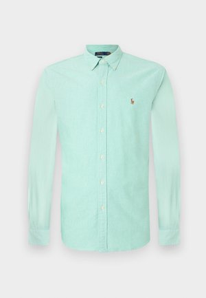 Mündroheline pikka varrukatega nööbiga särk, millel on krae, vasakul rinnal väike tikitud logo ja valged nööbid. Puuvillane kangas.