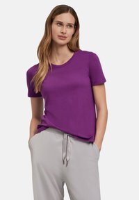 Paarse t-shirt met korte mouwen en ronde hals, gemaakt van een gladde stof. Gecombineerd met lichtgrijze joggers metkoord, die een ontspannen pasvorm laten zien.