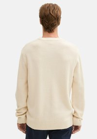 Crème gebreide trui met een textuurpatroon, geribde manchetten en een ronde halslijn, weergegeven van de achterkant.