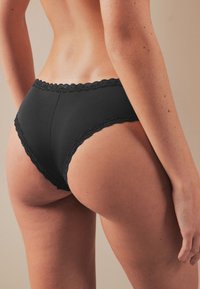 Culotte noire bordée de dentelle avec une coupe taille haute, présentant une texture lisse et une taille moyenne, arborant une ceinture élastique simple.