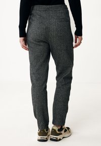 Šedé herringbone kalhoty s úzkým střihem, s vysokým pasem a zadní kapsou. Spárováno s teniskami v béžové a černé barvě.