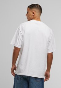 White cotton T-shirt with a loose fit, short sleeves, and a round neckline. The fabric has a soft texture and minimal seams for a clean look.