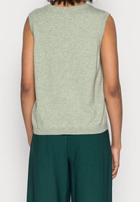 Haut sans manches en tricot vert avec un col et un ourlet côtelés, offrant une coupe décontractée et une texture lisse. Pas de détails supplémentaires.