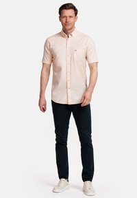 Korte mouwen, lichtroze overhemd met knoopsluiting en een zak, gecombineerd met donkere broek en witte sneakers. Glad materiaal, klassieke kraagontwerp.