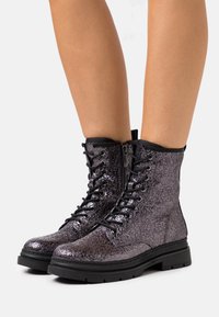 Bottines montantes en dentelle noire métallique avec une finition texturée, semelle en caoutchouc et détail de couture renforcée le long de la tige.