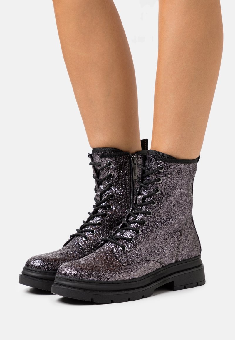 Bottines montantes en dentelle noire métallique avec une finition texturée, semelle en caoutchouc et détail de couture renforcée le long de la tige.