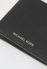 Zwarte leren portemonnee met een gestructureerd oppervlak en het zilveren "MICHAEL KORS" logo in reliëf op de voorkant. Compact ontwerp met strakke lijnen.