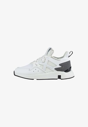 Chaussures de sport blanches avec des panneaux en mesh, des accents gris et une semelle blanche épaisse. Elles présentent des lacets, des détails de couture et une languette à l'arrière du talon.