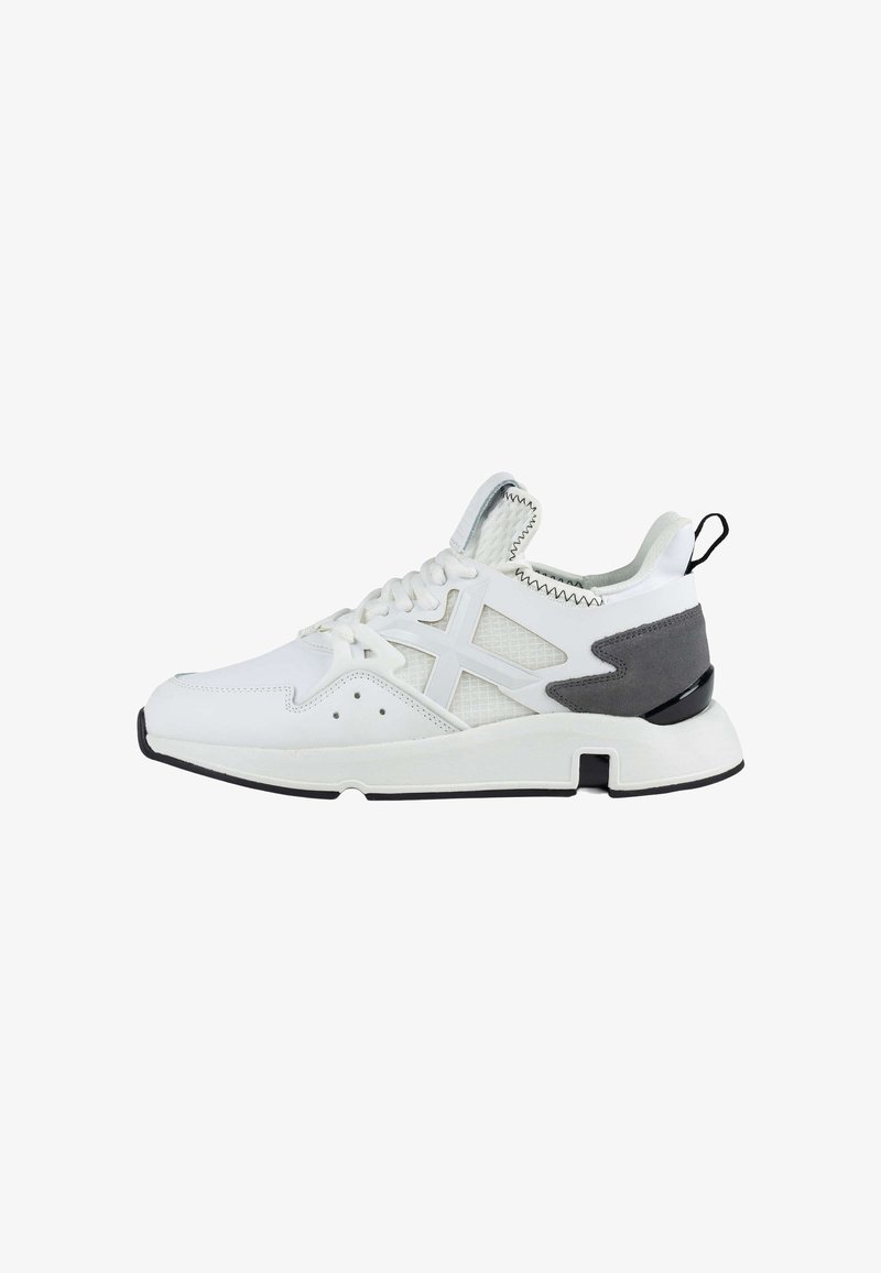 Chaussures de sport blanches avec des panneaux en mesh, des accents gris et une semelle blanche épaisse. Elles présentent des lacets, des détails de couture et une languette à l'arrière du talon.