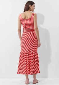 Rot-weiß gestreifter, ärmelloser Maxikleid mit einem taillierten Oberteil, ausgestelltem Rüschensaum und einem passenden Gürtel in der Taille. Glatte Stofftextur.