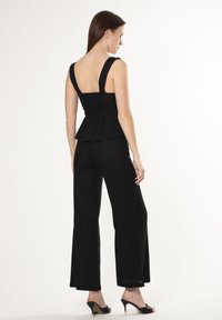 Top nero a peplum con spalline larghe, corpino arricciato, abbinato a pantaloni neri larghi. Il materiale sembra leggero, creando una silhouette rilassata.