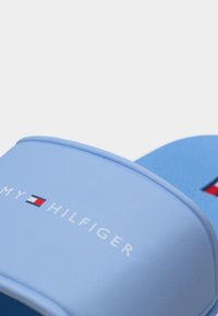 Ανοιχτού γαλάζιου χρώματος σανδάλια με λουράκι που φέρει το λογότυπο Tommy Hilfiger και έμβλημα με τη σημαία σε κόκκινο, λευκό και μπλε χρώμα.