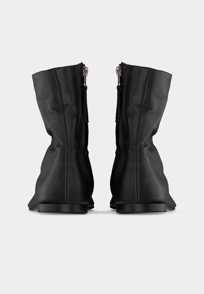 Ζευγάρι μαύρες δερμάτινες μπότες μέσης γάμπας με φερμουά ρ στο πίσω μέρος, εμφανιζόμενες από πίσω σε λευκό απλό φόντο.
