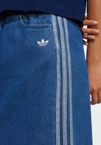 Denimskjørt i blått, med hvit tre-stripe design og en liten hvit logo. Inkluderer en fremre lomme og en teksturert overflate.