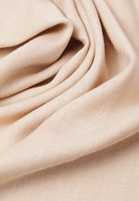 Helebeige kangas pehmea tekstuuriga, millel on peened diagonaalsed sooned, rippumas õrnades voldikutes, rõhutades selle paindlikku iseloomu.