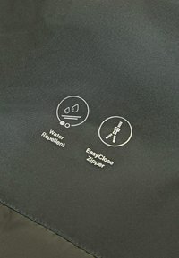 Tessuto nero con icone per impermeabile e cerniera facile da chiudere. La texture appare liscia con una leggera lucentezza.