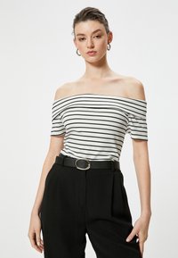 Off-shoulder stribet top i hvidt og sort stof, med korte ærmer og en tætsiddende design, parret med højtaljede sorte bukser og et bælte.