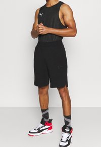 Černý bezrukávový top s jemnou síťovinou, spárovaný s černými kraťasy s logem. Obuv tvoří černé, bílé a červené vysoké tenisky.