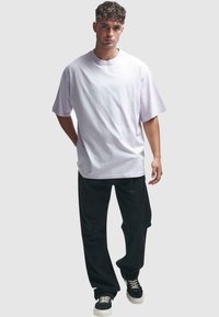 Lys lilla oversized t-shirt, lavet af bomuldsstof, rund hals, korte ærmer, parret med sorte løstsiddende bukser og sorte sneakers med hvid sål.