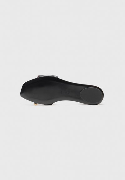 Chaussure plate noire avec une texture lisse et un bout arrondi. Équipée d'une sangle métallique et d'un logo discret sur la semelle. Design minimaliste.