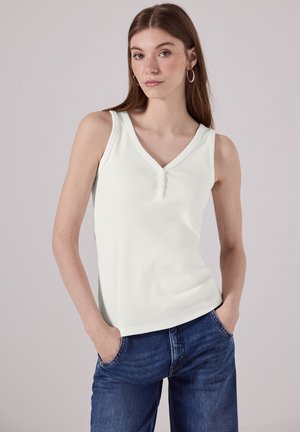 Haut sans manches blanc avec un décolleté en V, présentant une texture côtelée et deux boutons à l'avant. Associé à un jean en denim bleu.