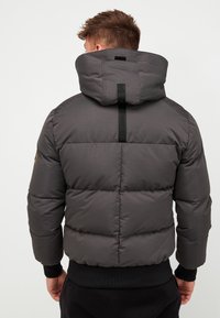 Gray puffer jacket with a high collar, featuring horizontal stitching, elastic cuffs, and a black accent strap along the back.