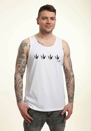 Biały bawełniany top na ramiączkach z czarnym graficznym wzorem korony na piersi; model ma widoczne tatuaże i nosi szare dżinsy.