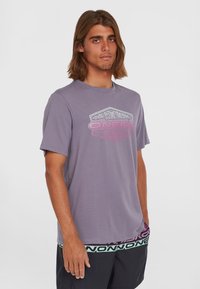 Kortærmet, lys lilla T-shirt med et grafisk logo i pink og hvid, med en rund halsudskæring og blød, glat tekstur.