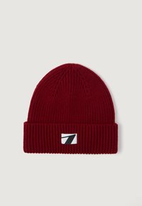 Gorro de punto rojo con textura acanalada, dobladillo doblado y una etiqueta rectangular con fondo blanco y gráfico negro.
